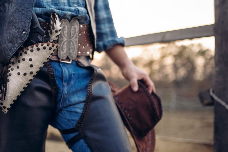 Studded leather chaps, a belt buckle and a hat held at the hip